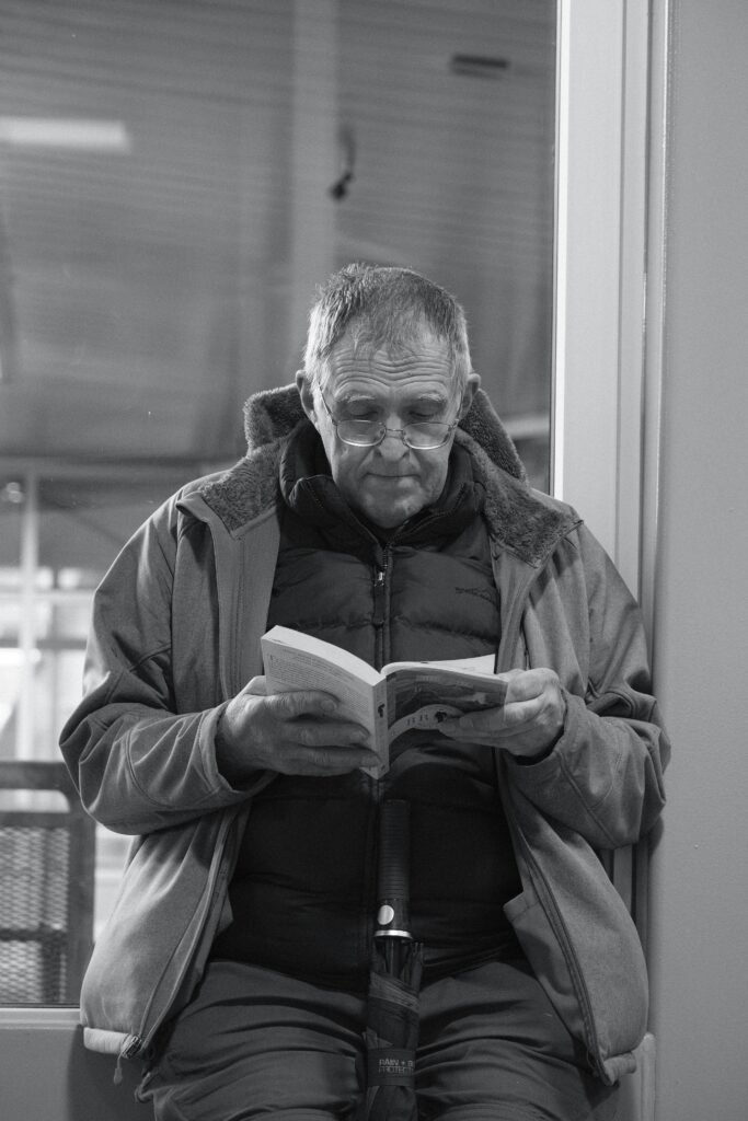 Senior man in a jacket reads a book indoors in a calm setting.